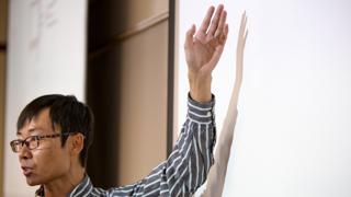 一个亚洲人站在黑板前讲课的侧面照片.